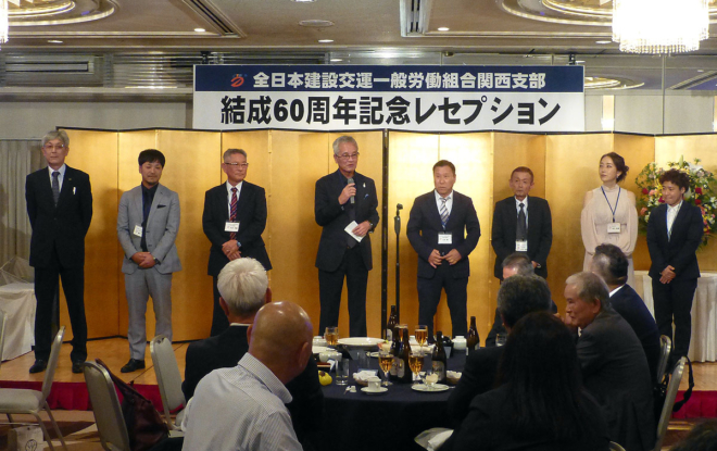 実行委員会のメンバーが紹介された。左から副執行委員長の森田昌志氏、書記長の藤川拓氏、執行委員長の本多裕重氏、顧問の岡元貞道氏、副執行委員長の北村彰氏、副執行委員長の山内真樹氏、事務局の圓尾知恵氏、事務局の金丸涼子氏。