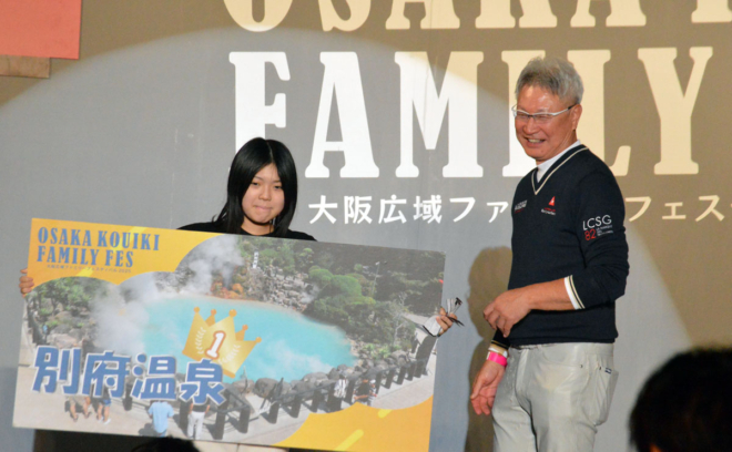 大人の部・1等の＜別府温泉＞を当てて大喜びの参加者と、プレゼンターの木村理事長。